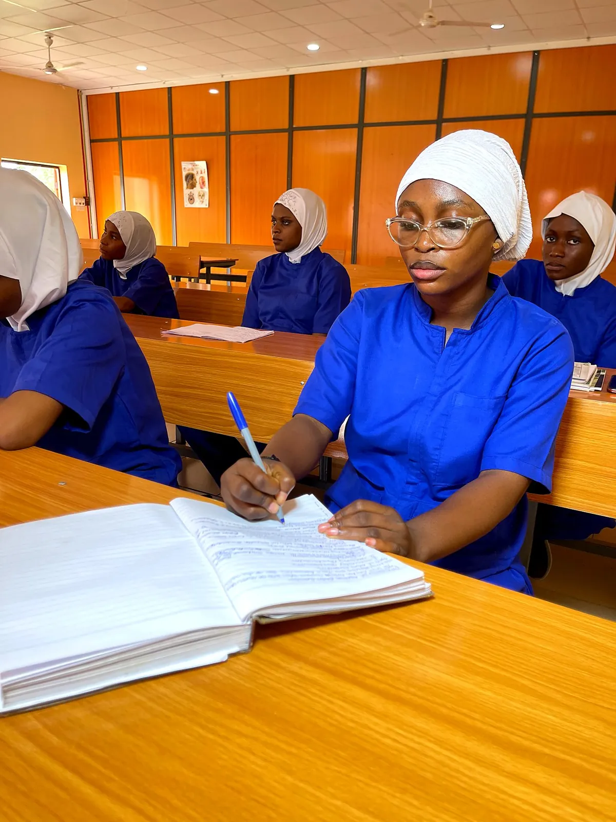 Student nurse in blue scrubs taking notes in the lecture hall