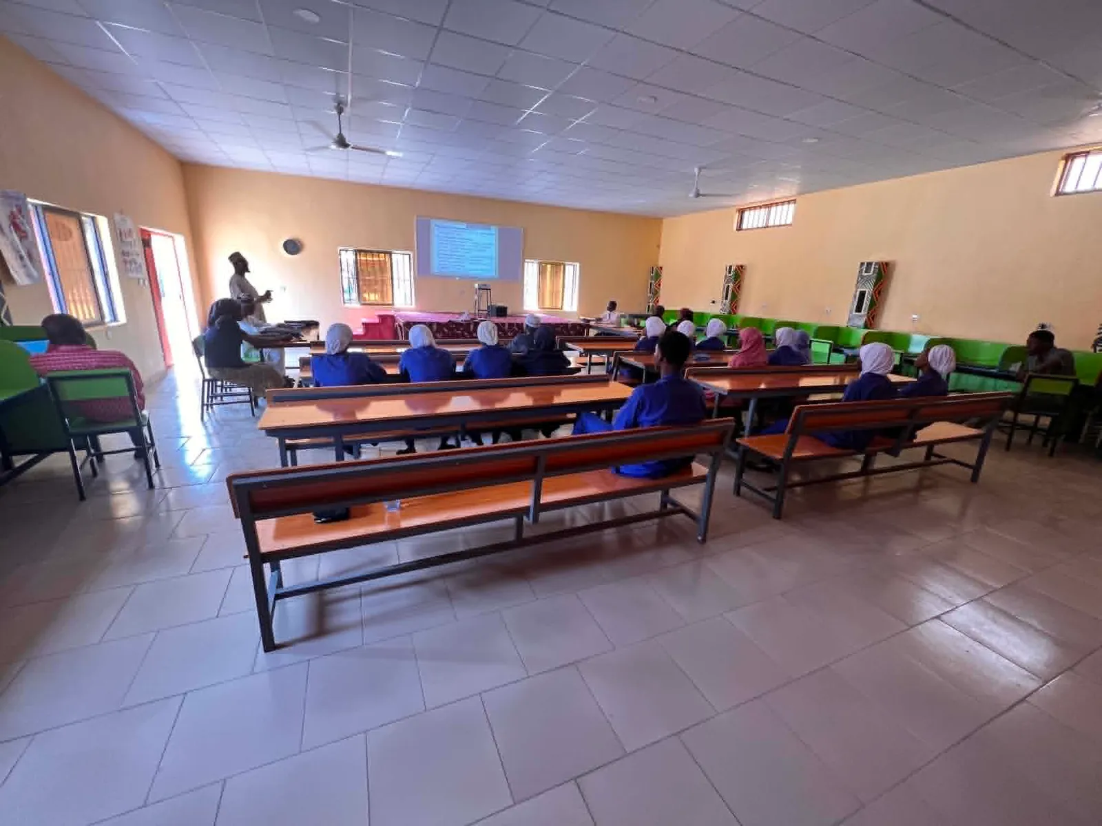 A lecture in progress in the college lecture hall, students at bench desks facing a projected slide